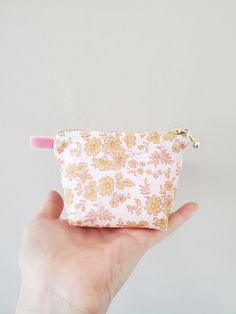 a hand holding a small pink and yellow flowered pouch with a zipper on it