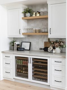 a kitchen with white cabinets and shelves filled with wine bottles, glasses and other items