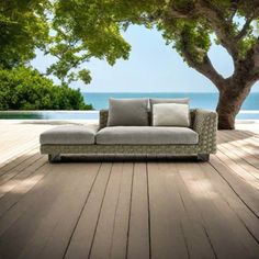 a couch sitting on top of a wooden floor next to a tree and the ocean