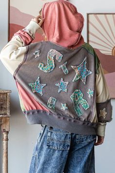 a woman wearing a hoodie with sequins and stars on it, standing in front of a wall