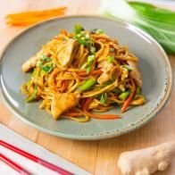 a plate full of noodles and chicken with chopsticks next to it on a cutting board