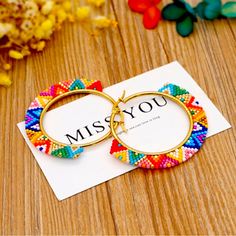 two colorful hoop earrings with the word miss you printed on them, sitting next to some flowers