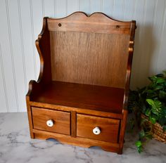 a wooden bench with two drawers on top of it next to a potted plant