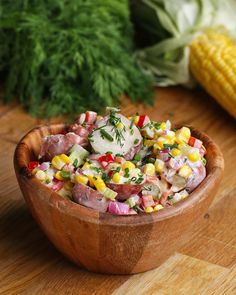 a wooden bowl filled with salad next to corn on the cob