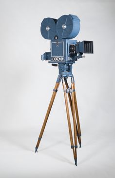 an old fashioned movie camera on a tripod with wooden legs and two cameras attached to it