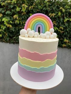 a rainbow cake with white frosting and sprinkles on top is being held by a person