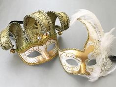 A polarizing combination where the man wears the white/gold Jester mask and the woman looks elegant in the white/gold Venetian mask, which comes attached with feathers and a flower. White Costume Mask For Mardi Gras, White Mardi Gras Costume Mask, White Masquerade Masks And Prosthetics For Mardi Gras, White Mardi Gras Masquerade Masks And Prosthetics, White Masks And Prosthetics For Mardi Gras Masquerade, White Masks For Mardi Gras Costume Party, White Masquerade Mask For Mardi Gras Costume Party, White Venetian Masquerade Mask For Mardi Gras, Elegant White Costume Mask