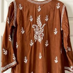 This Brown Muslin Silk Lucknowi Chikankari Kurta Hand Embroidered is a unique piece of clothing. It features a straight long finish along with straight hems. The back and sleeves of the kurta are decorated with loosely scattered motifs, while the front is enhanced with dense embroidered neck and motifs. This product is a must-have for anyone looking for a unique and stylish formal wear piece. Pair it with our chikankari sharara or white cotton pants for an effortless chic look. Length 42" inches Brown Chikankari Kurta, Chikankari Sharara, Phulkari Pants, White Cotton Pants, Lucknowi Kurta, Patiala Salwar Suits, Chikankari Kurta, Bridal Dupatta, Phulkari Dupatta