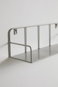 a metal shelf mounted to the side of a white wall with two hooks on it