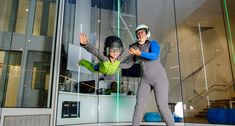 two people wearing helmets and bodysuits standing in front of a glass building