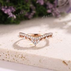 a diamond ring sitting on top of a piece of white marble with purple flowers in the background