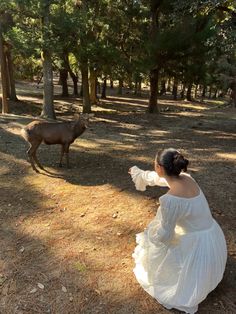 a woman in a white dress kneeling down next to a brown animal on the ground