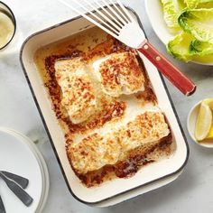 a pan filled with lasagna covered in cheese and sauce next to plates of salad