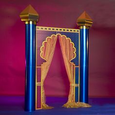 an elaborate blue and gold wedding arch with curtains on the sides, in front of a pink backdrop