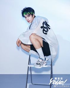 a young man sitting on top of a chair with his legs crossed and green hair