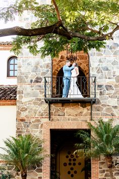 a man and woman standing on the balcony of a building with trees in front of them