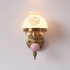 a wall mounted light on the side of a white wall with a pink ball hanging from it