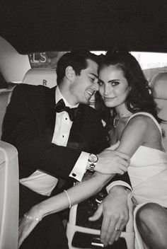 a man in a tuxedo and a woman in a white dress sitting on a car seat