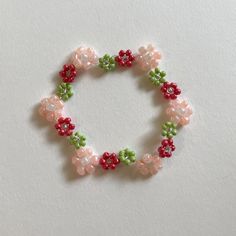 a beaded bracelet with pink and green flowers on the clasp, sitting on a white surface