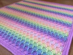 a multicolored crocheted blanket sitting on top of a wooden floor next to a table