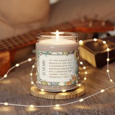 a lit candle sitting on top of a wooden table next to a string of lights