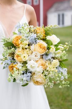 a bride holding a bouquet of flowers in her hand on the grass near a barn