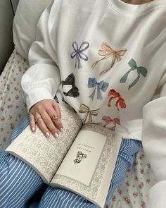 a woman sitting in bed holding an open book with bows on it's sleeves