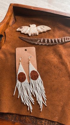 two pairs of earrings are sitting on top of a leather tray with feathers and beads