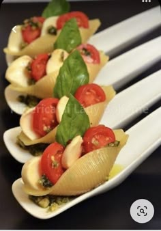 four pasta shells with tomatoes and spinach on white serving utensils, ready to be served