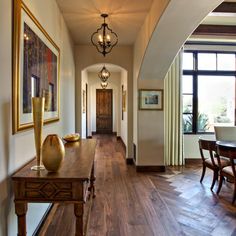 a long hallway with wood floors and chandelier hanging from the ceiling next to a dining room table