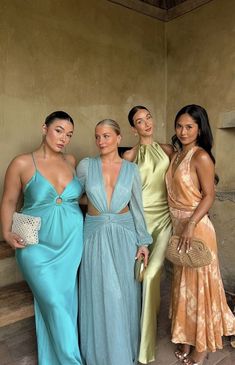 four beautiful women standing next to each other in long dresses and one is holding a purse