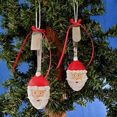 two christmas ornaments hanging from a tree with red ribbon and santa's head on them