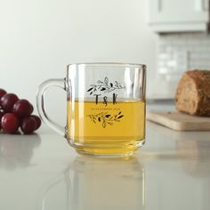 a glass mug sitting on top of a counter next to some bread and grapes in the background