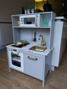 a toy kitchen set with sink, stove and microwave in the middle on wooden flooring