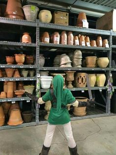 a woman in a green jacket and some shelves with pots