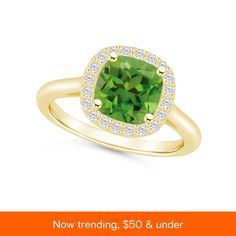 an engagement ring with a green cushion cut stone surrounded by diamonds on the band and in yellow gold