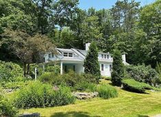 a large white house surrounded by trees and bushes in the middle of a wooded area