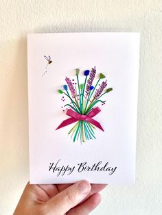 a hand holding up a card that says happy birthday with purple flowers and red ribbon