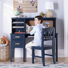 a young boy sitting at a desk in front of a book shelf