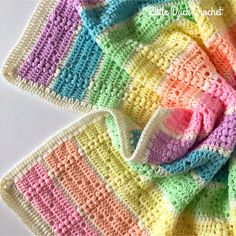 a crocheted blanket is laying on top of a white surface with multicolored squares