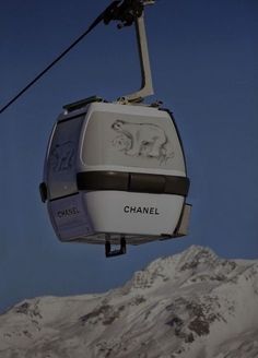 a cable car with the word chanel on it in front of snow covered mountains