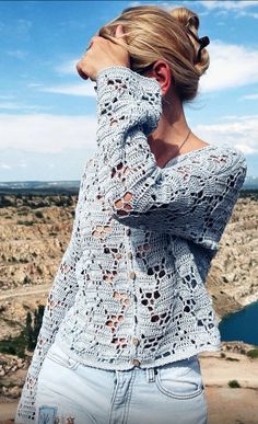 a woman standing on top of a hill next to a lake wearing a sweater and jeans