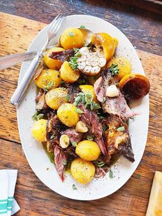 a white plate topped with lots of food on top of a wooden table next to utensils