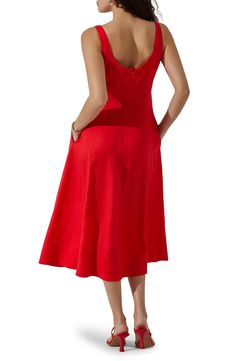 a woman in a red dress is looking back at the camera and she has her hands on her hips