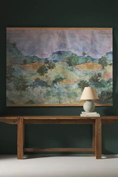 a painting hanging on the wall next to a wooden table with a lamp on it