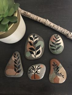 four painted rocks sitting on top of a table next to a plant