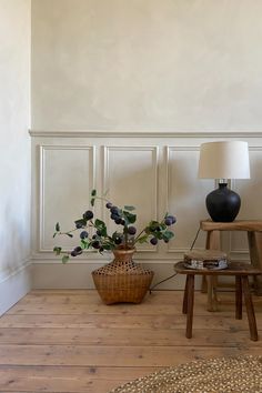 a room with a chair, table and vase on the floor next to a lamp