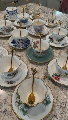 there are many tea cups and saucers on the table with spoons in them