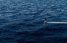 a person sitting on the edge of a boat in the middle of the ocean,