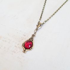 A classic and dainty art nouveau style antiqued brass pendant with a vintage ruby red Czech glass cabochon is suspended from an antique bronze chain. Choose your length in inches from the drop down menu. The pendant measures 1 1/2 inches (37 mm) from top to bottom, including the decorative connector. It is a quality USA made vintage style brass pendant with a lightly antiqued finish. The bright ruby red glass cabochon is vintage Czech glass. The antique bronze plated chain has a lobster clasp an Vintage Red Round Pendant Jewelry, Antique Red Oval Pendant Jewelry, Elegant Red Brass Necklace, Vintage Red Cabochon Necklace, Vintage Red Oval Pendant Necklace, Red Vintage Necklace With Cabochon, Red Vintage Cabochon Necklace, Art Nouveau Necklace With Vintage Charm For Gifts, Red Oval Pendant Vintage Necklace